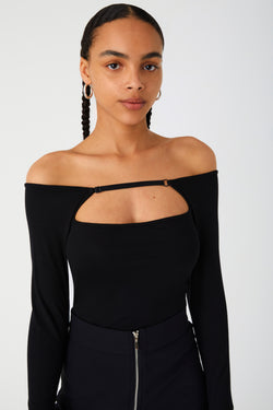 Woman in a chic off-the-shoulder top with a unique neckline. Top has strap connecting sleeves over the chest, leaving an open cut out across the high bust.