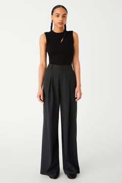 Woman modeling a chic black sleeveless top and elegant grey wide-leg trousers. Pants are dark charcoal colour with white pinstripes. Pants are an oversized fit, with oversized centre pleats.