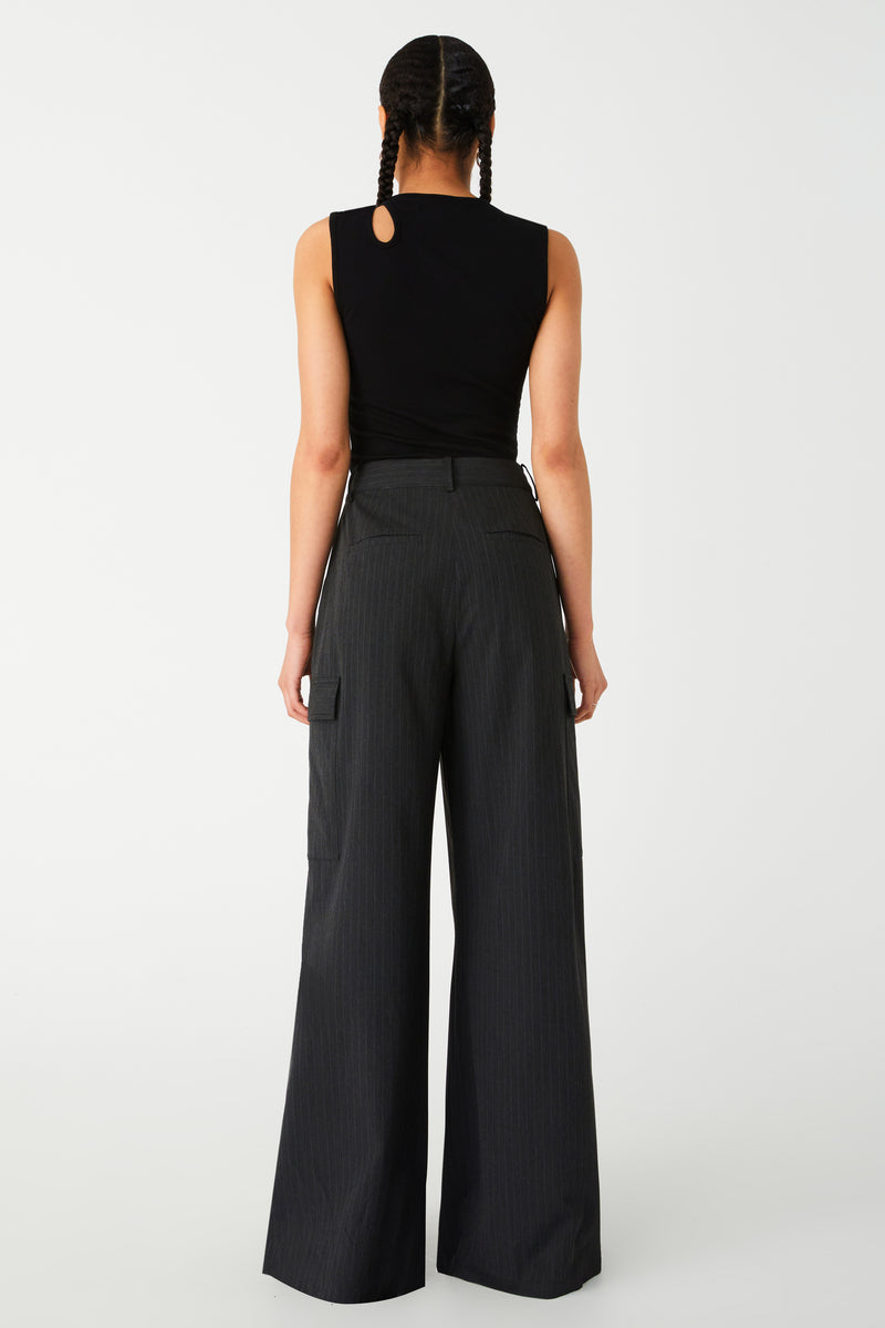 Woman modeling a chic black sleeveless top and elegant grey wide-leg trousers. Pants are dark charcoal colour with white pinstripes. Pants are an oversized fit, with oversized centre pleats.