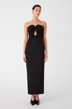 Woman posing in a black strapless gown with a front cut-out detail. Dress is maxi length with ruching around bust and curved strapless neckline.