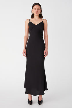 Girl with short hair in satin Black maxi dress. Dress has a v-neck with ruched detailing on the bust seems and thin spaghetti straps.