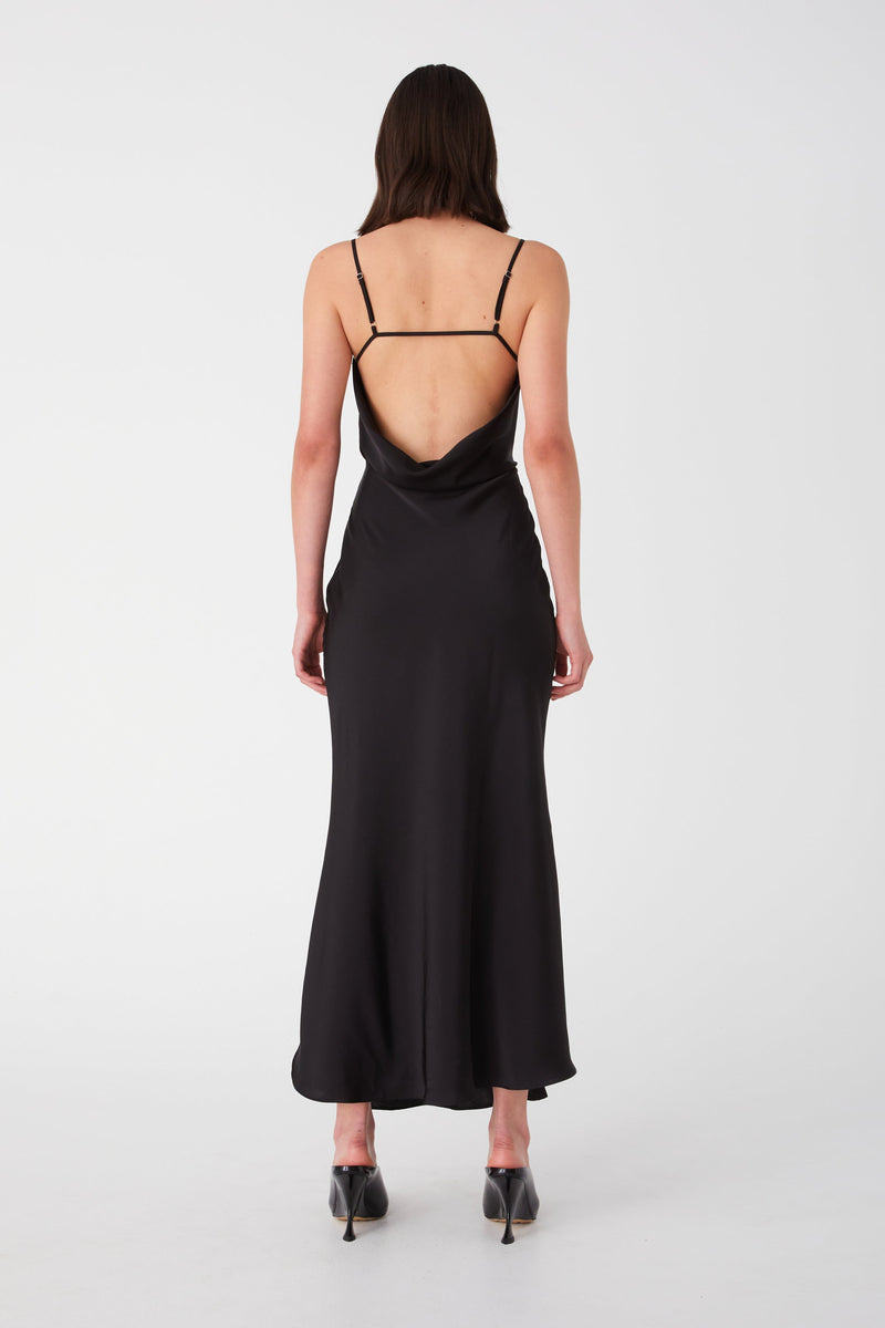 Girl with short hair in satin Black maxi dress. Dress features a draped low back detail and thin spaghetti straps crossing on the upper back.