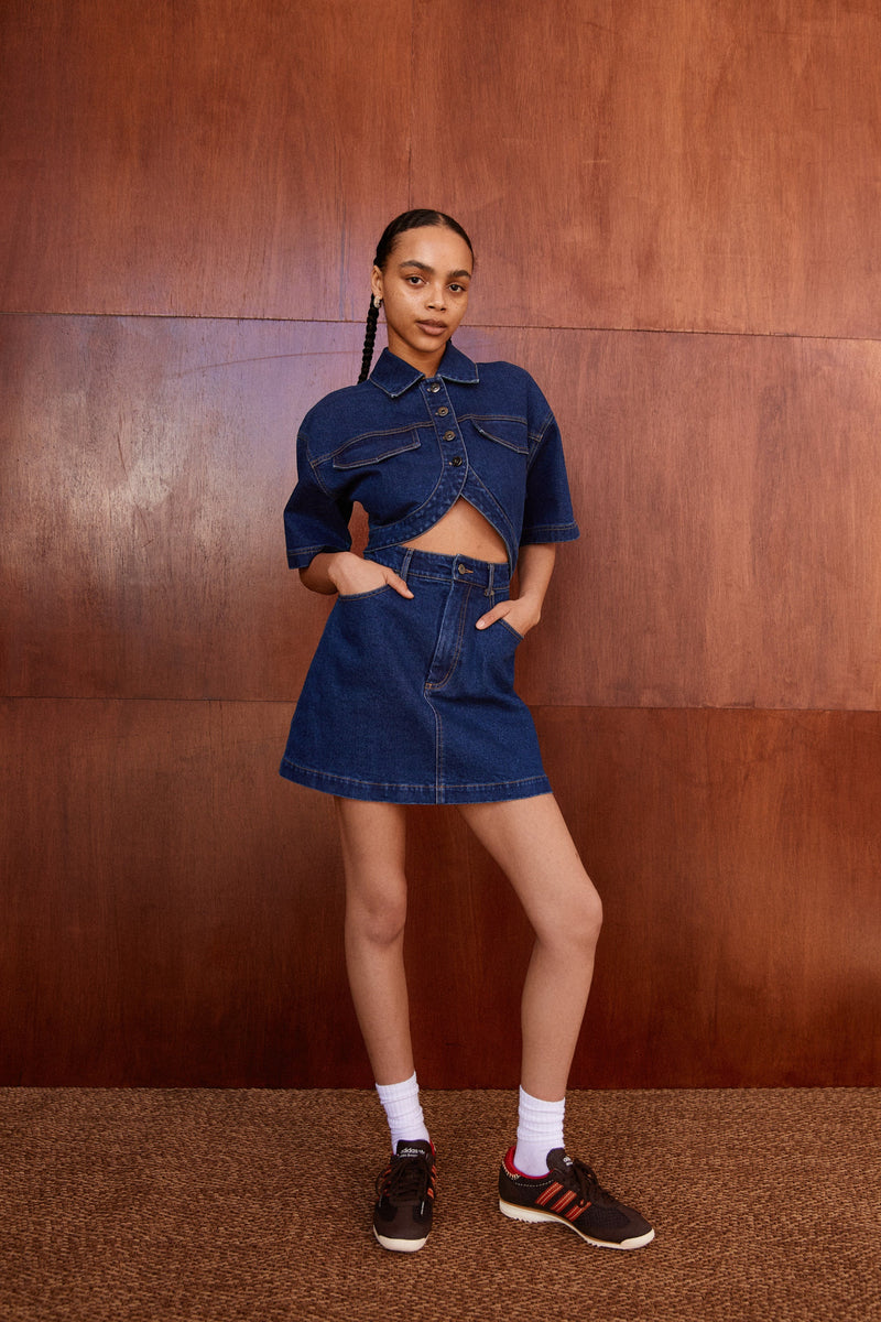 Girl in denim mini dress with middle cutout. Dress features collar, buttons, oversized sleeves and curved hem
