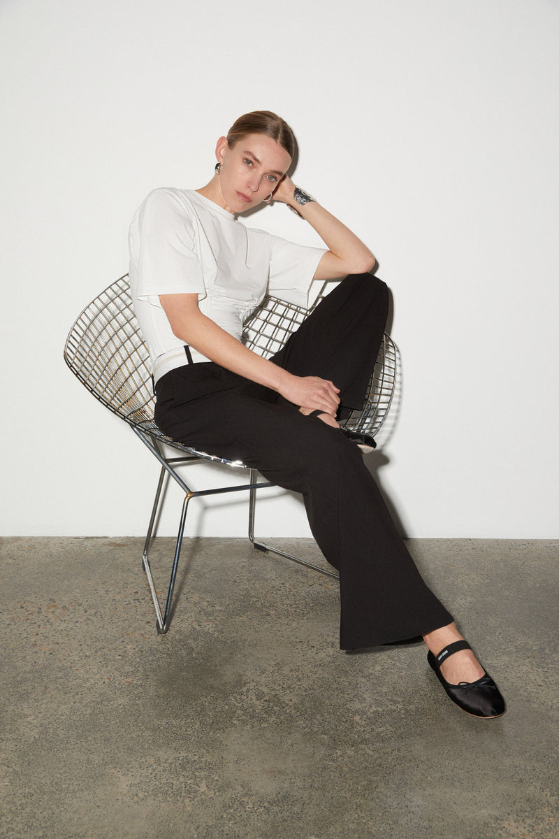 Girl sitting down in Black long pants with white fold-over waistband and front pleats. Worn with white tee-shirt with corset detailing.