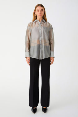 Woman in sheer silver button down shirt. Shirt is oversized. Styled with black pants and black heels.