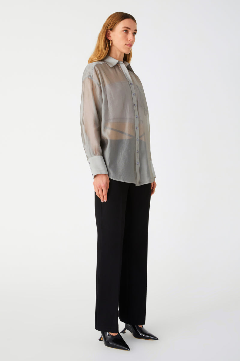 Woman in sheer silver button down shirt. Shirt is oversized. Styled with black pants and black heels.