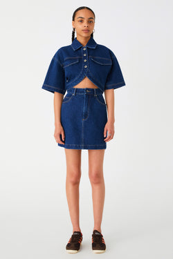 Girl in denim mini dress with middle cutout. Dress features collar, buttons, oversized sleeves and curved hem