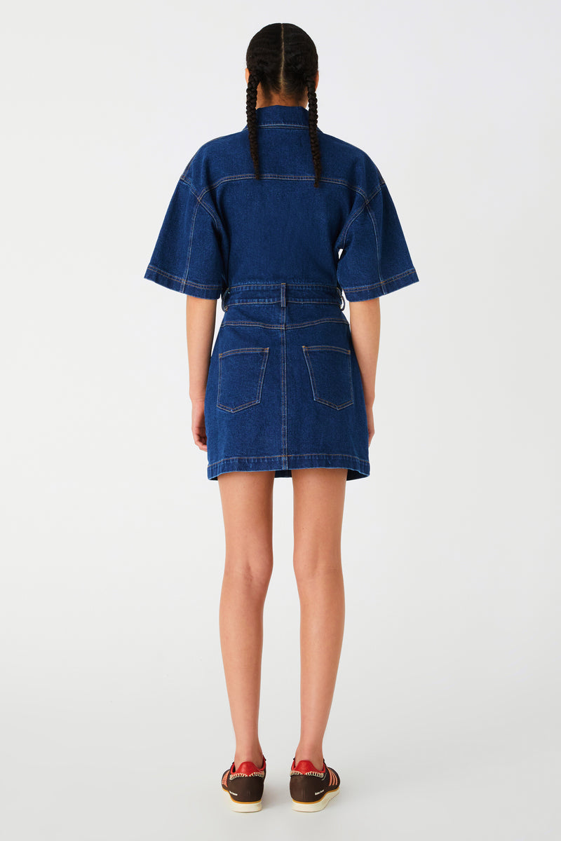 Girl in denim mini dress with middle cutout. Dress features collar, buttons, oversized sleeves, back pockets and curved hem