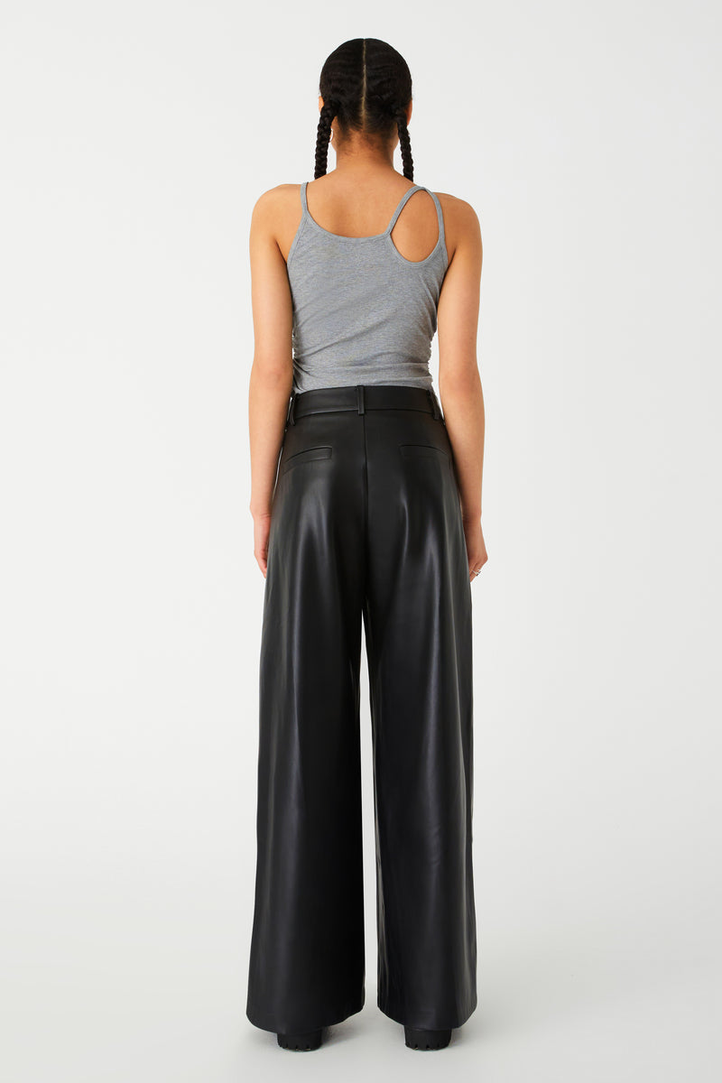Woman in a stylish grey tank top and black wide-leg leather pants. Grey Tank features unique strap detailing, with slight cutout and double strap on shoulder.
