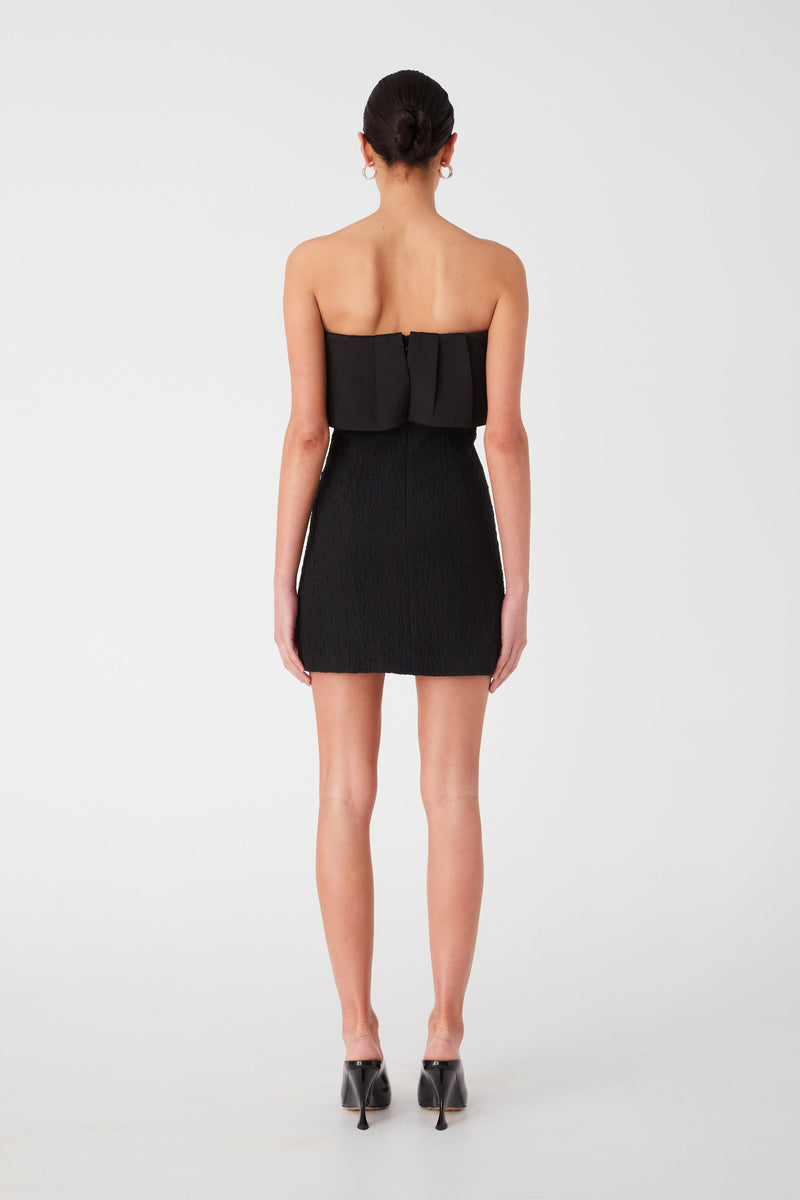 Black strapless mini dress with bandeau fold over detail. Dress is A-line and worn with black heels.