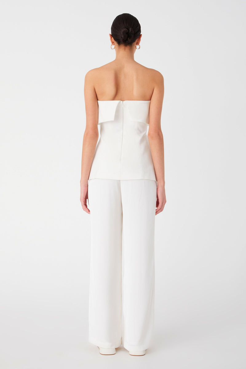 Girl wearing white strapless top with bandeau fold over detail. Top is longline and is worn with white long pants.