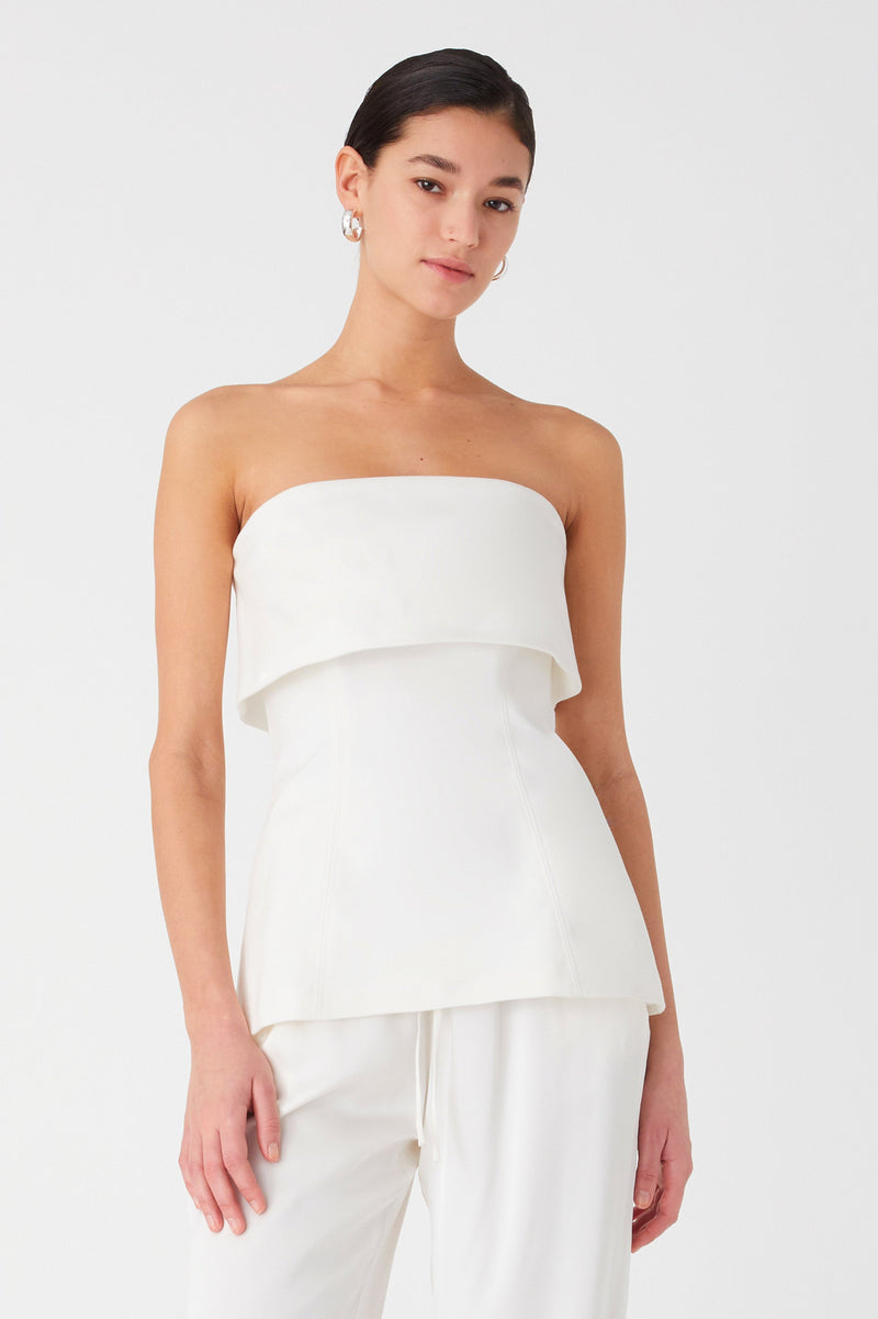 Girl wearing white strapless top with bandeau fold over detail. Top is longline and is worn with white long pants.