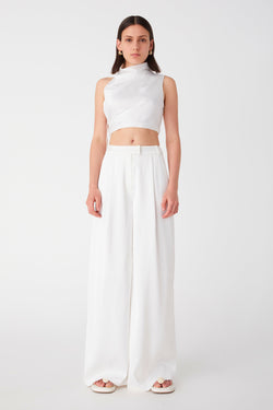 Girl wearing oversized long white pants. Pants have large front pleats and a suiting waistband. Worn with satin high neck crop top and white sandals.