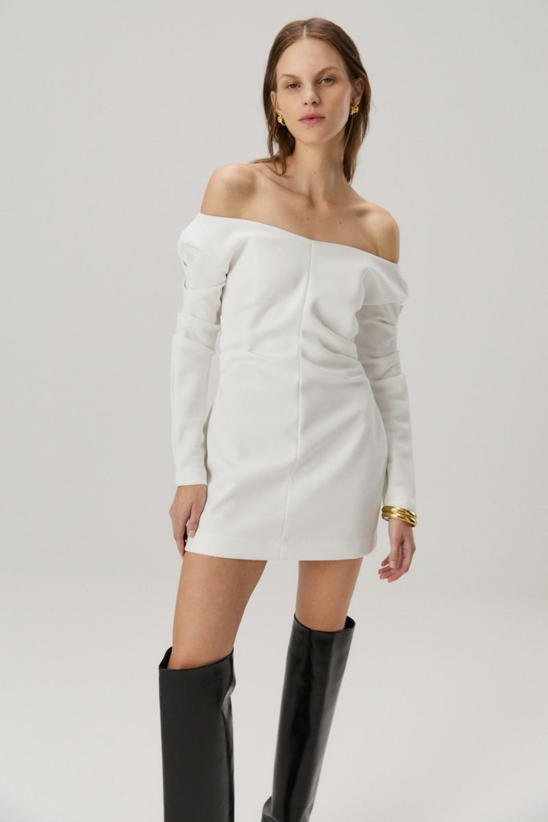 Girl with blonde hair wearing a bonded crepe dress in ivory. The dress features off the shoulder long sleeves