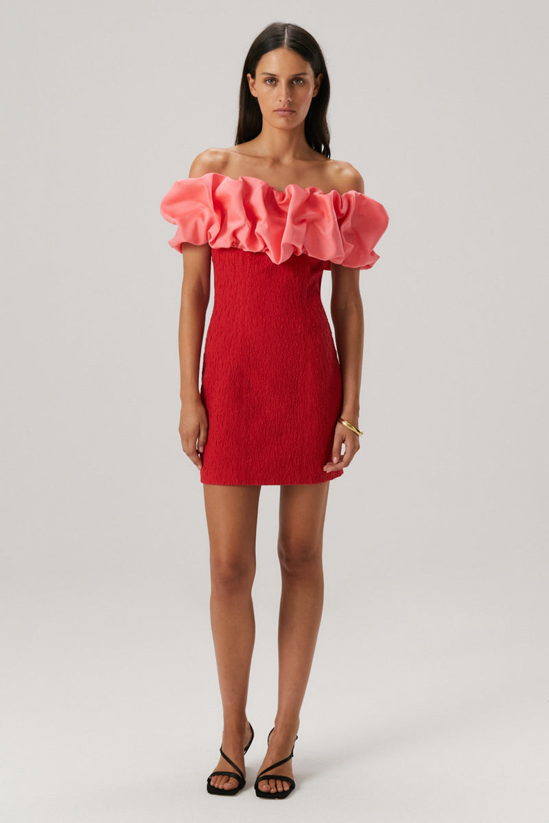 Girl wearing a red rouched bodycon mini dress featuring an off the shoulder pink ruffle sleeve