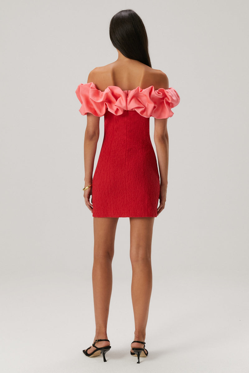 Girl wearing a red rouched bodycon mini dress featuring an off the shoulder pink ruffle sleeve