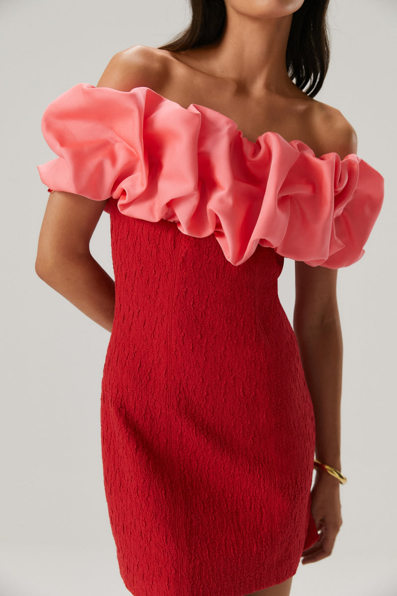 Girl wearing a red rouched bodycon mini dress featuring an off the shoulder pink ruffle sleeve